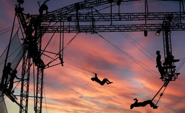 silhouettes of trapeze artists acrobats on the metal scaffolding at sunset