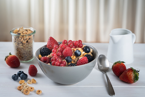 Cereal bowl with berries and milk on a white table. Healthy eating concept. Front view.