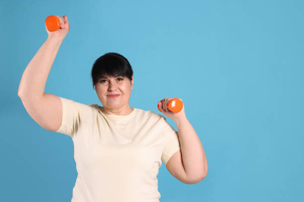 istock Happy overweight mature woman doing exercise with dumbbells on light blue background, space for text 1454155974