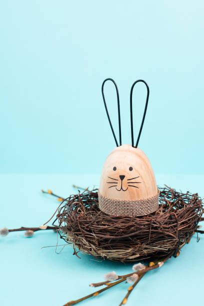 istock Easter bunny or rabbit sitting in a bird nest, willow branches, wooden egg, spring holiday, brown and blue color 1454157953