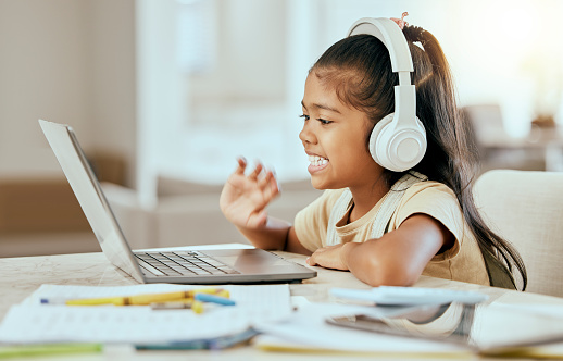 Video call, online education and child with laptop, headphones and home table for e learning virtual class. Hello, zoom call and girl kid in elearning school listening to audio kindergarten language