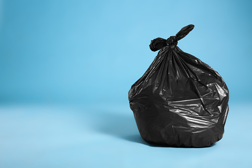 Black trash bag full of garbage on light blue background, space for text