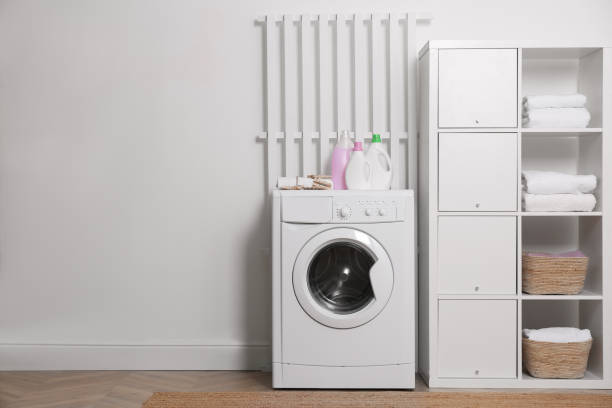 istock Laundry room interior with modern washing machine and shelving unit near white wall 1454158915