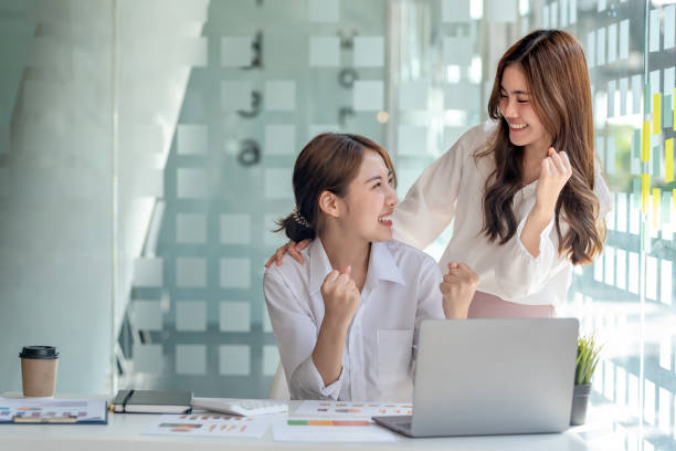 Successful young Asian business woman achieving goals excited raised hands rejoicing with laptop in the office. New startup project concept. stock photo