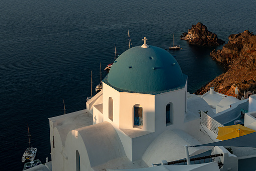 View at sunrise of one of the famous blue domes and Aegean ocean in Oia, Santorini.