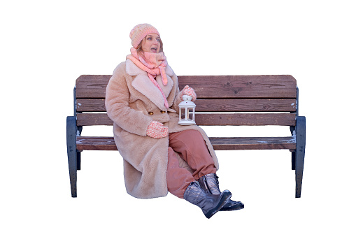 A happy woman is sitting on a bench with a lantern in her hands, a winter park with snow-covered trees, isolated on a white background