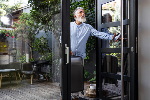 A senior man arrives at a rental flat. A man with a beard is carrying a suitcase.