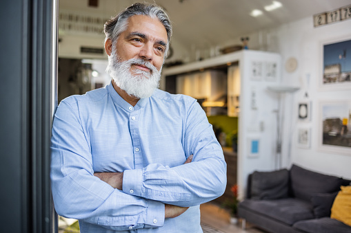 Portrait of a bearded senior man with arms crossed at home. Contemplation. Copy space.