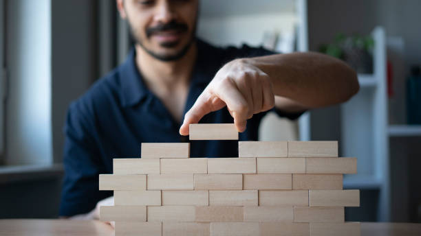 Happy man builds wall from wooden blocks