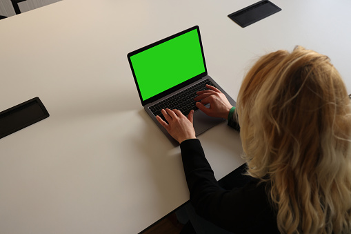 Woman using laptop on table with green screen