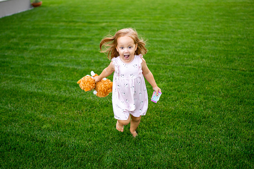 a wide shot of a little girl running barefoot on the green grass having sun, smilling.