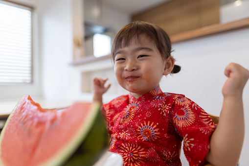 Happy little girl wearing yukata eating watermelon in dining room