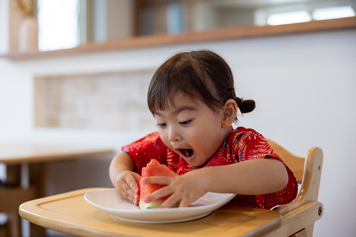 Happy little girl wearing yukata eating watermelon in dining room