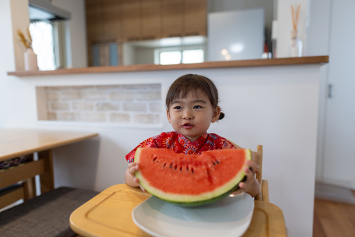 Little girl wearing yukata eating watermelon in dining room