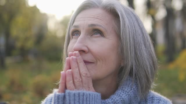 Grateful senior woman raising eyes to sky asking god for blessing and healing