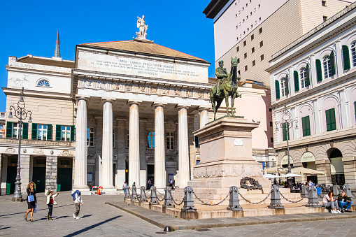 People strolling in Largo Sandro Pertini in the downtown of Genoa, where overlooks the Teatro Carlo Felice, the principal city opera house, and where stands out the Monument to Garibaldi, work dated 1893 by the sculptor Augusto Rivalta