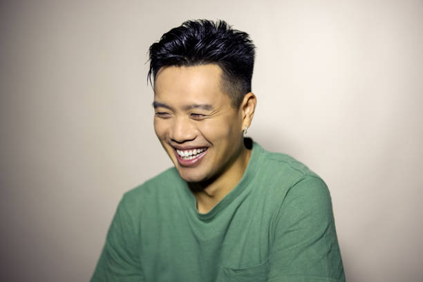 Close-up portrait of cheerful young man on grey background. Asian male in green t-shirt looking down and smiling in studio.