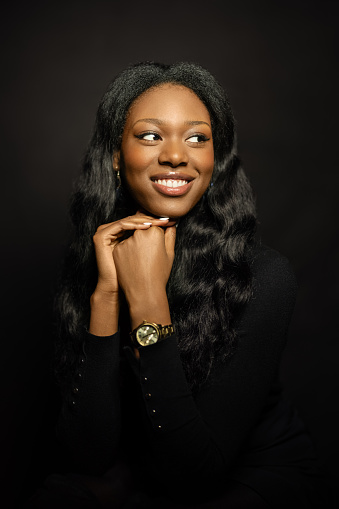Portrait of pretty young African woman on black background. Young female looking away and smiling in studio.
