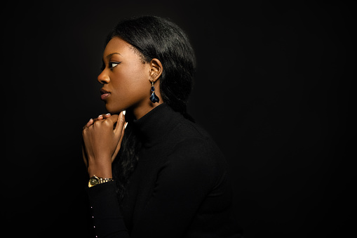 Side view of confident young woman on black background. African female model with hand on chin in studio.