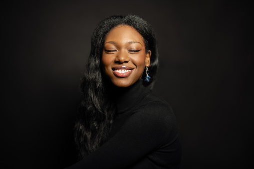 Studio portrait of african young woman with closed eyes and smiling. Beautiful woman smiling on black background.