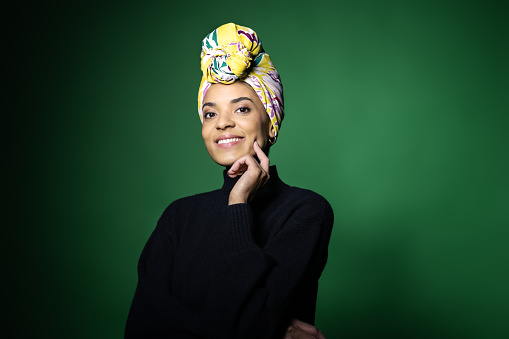 Portrait of attractive young african woman on green background. African female with a scarf wrapped on head looking at camera and smiling.