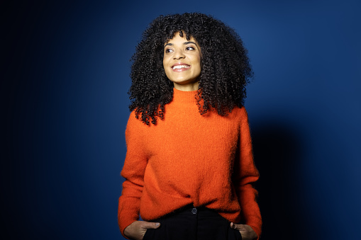Portrait of beautiful young woman in red sweater. Happy woman with curly hair looking away and smiling against blue background.