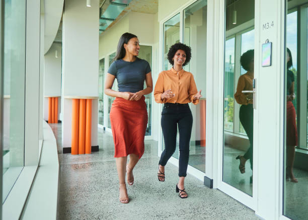 istock Diverse young businesswomen talking while walking along an office hall 1454186193