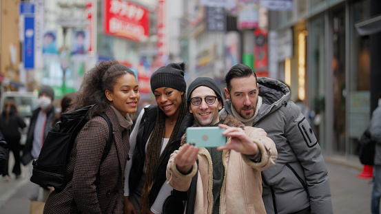 A multi-racial group of tourist friends are taking selfies and videos while exploring the city In Shibuya Tokyo.