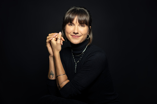 Portrait of attractive young woman against black background. Happy young female wearing black polo neck t-shirt looking at camera.