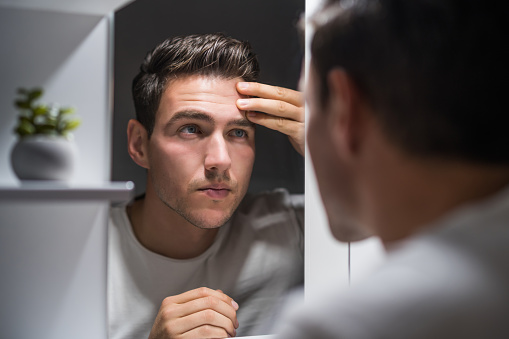 Man looking at his wrinkles while standing in front of mirror.
