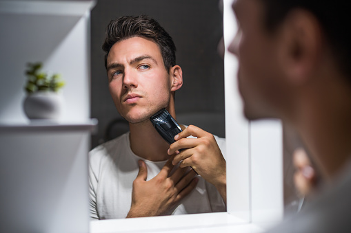 Man shaving  beard while looking himself in the mirror.