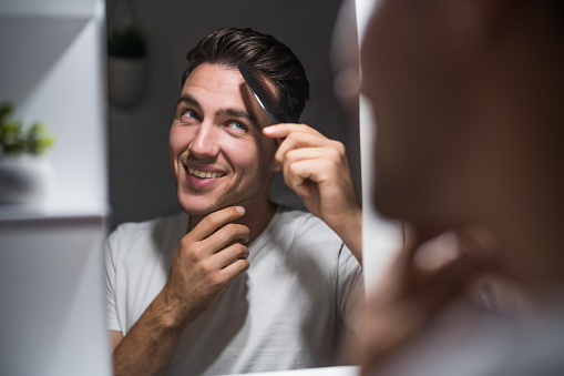 Man combing his hair while looking himself in the mirror.