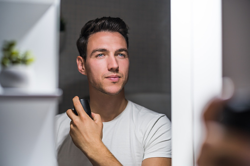 Man using deodorant  while looking himself in the mirror.