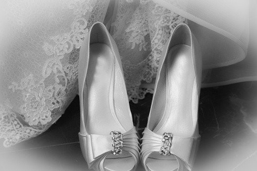 A greyscale closeup view of white bridal shoes and the veils of the bride