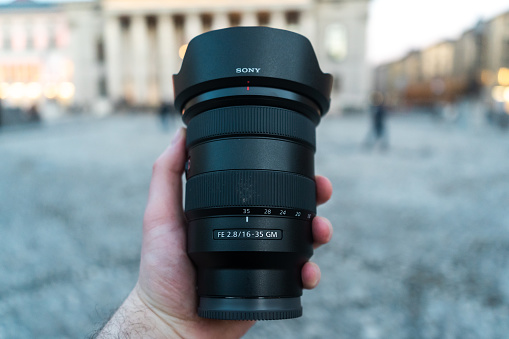 Munich, Germany – February 20, 2021: The Sony 16-35 f2.8 GM lens in front of an urban background. The professional wide angle lens is held by a male hand.