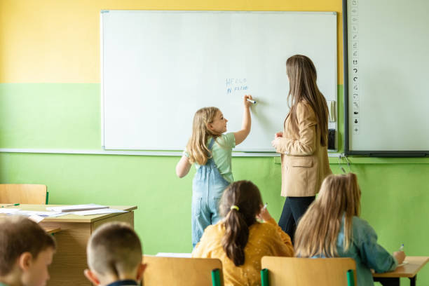 Female teacher and children in the classroom School children and female teacher during lesson in the classroom in the elementary school. Girl writing on the white board. kids using smart board stock pictures, royalty-free photos & images