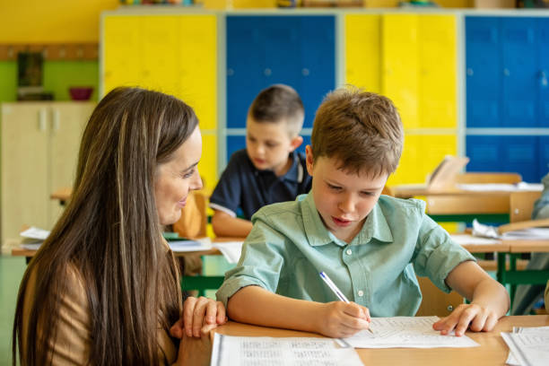 istock Female teacher helping boy during lesson 1454189336