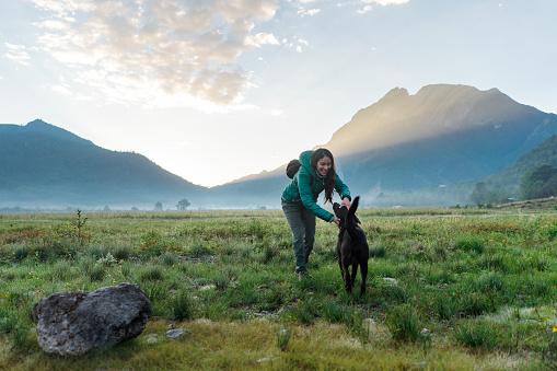 A young latin woman hiking outdoors and playing with her dog and sunrise.