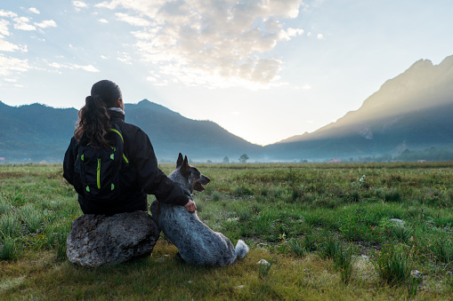 A young latin woman sitting on a rock next to her dog outdoors and looking at the view.