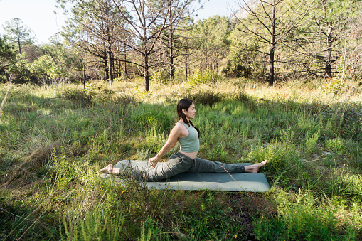 A young latin woman doing yoga and stretching her legs outside in a forest.