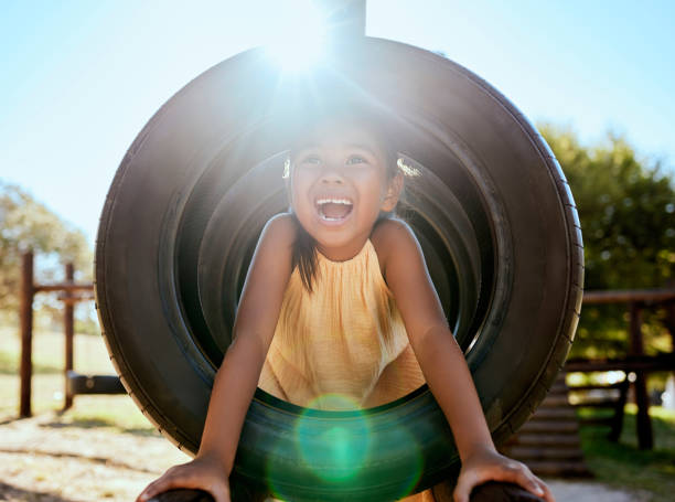 child, smile and park on jungle gym, tyre and playing in sunshine, summer and outdoor while excited. happy, girl and wow for laugh, happiness and playground in lens flare, comic and nature in orlando - child jungle gym playground laughing imagens e fotografias de stock