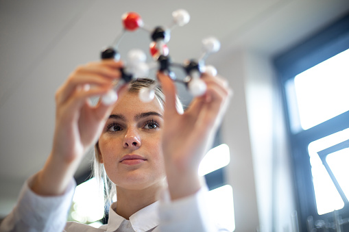 Close-up, shot through the hands of a female teenager examining a molecular chemistry set. She is wearing her school uniform.