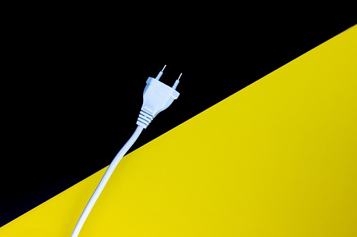A closeup shot of a white electrical plug with a wire on a yellow black surface