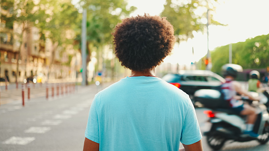 Close-up of young African American man in  light blue t-shirt is standing on crosswalk.