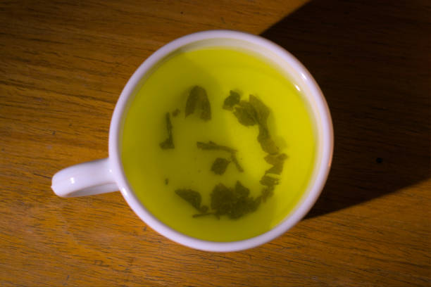 A cup of herbal or green tea with leaves on a table. Top view.