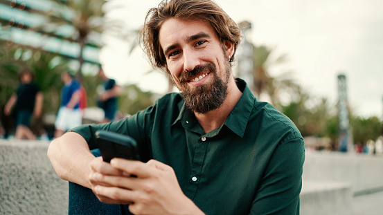 Close-up portrait of a man with a beard recording a voice message on the embankment background. Closeup of a young hipster male using a mobile phone