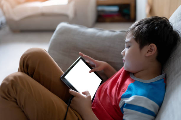 istock Happy Child with tablet computer. Portrait Kid Holding Digital Tablet With Empty Screen Mockup, Young boy sitting on sofa relaxing and playing with touch pad at home 1454196262