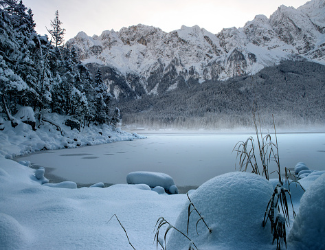 A frozen Eibsee river surrounded by trees covered with snow in Bavaria, Germany