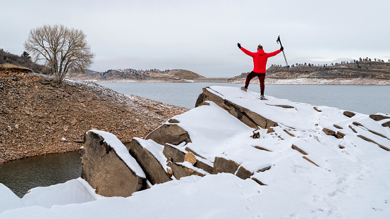 happy male hiker with trekking poles on a rocky shore of a mountain lake at foothills of Rocky Mountains, Horsetooth Reservoir - a popular recreational area in northern Colorado in winter scenery
