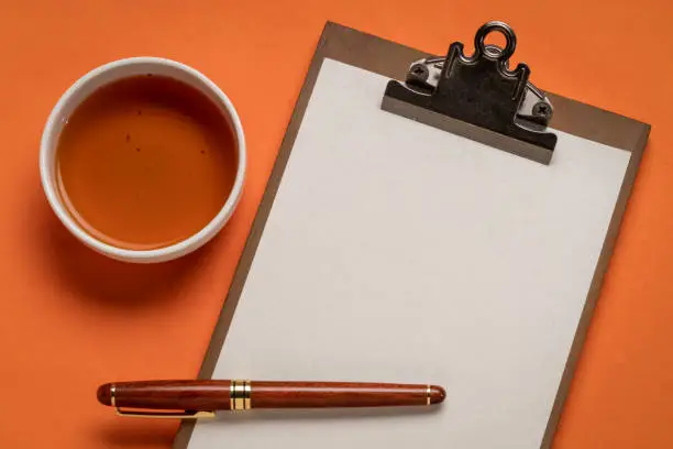 clipboard with a blank paper, desktop flat lay with a cup of tea and a stylish pen